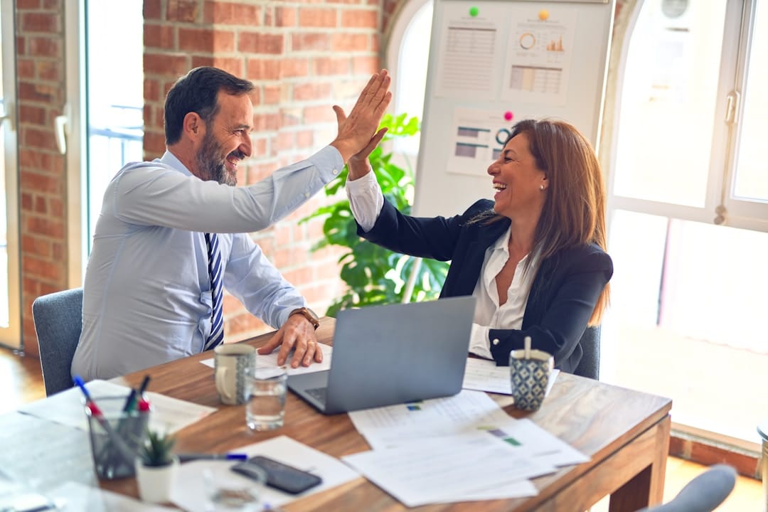 Two colleagues high-five after successful sales leadership helped reach sales goals