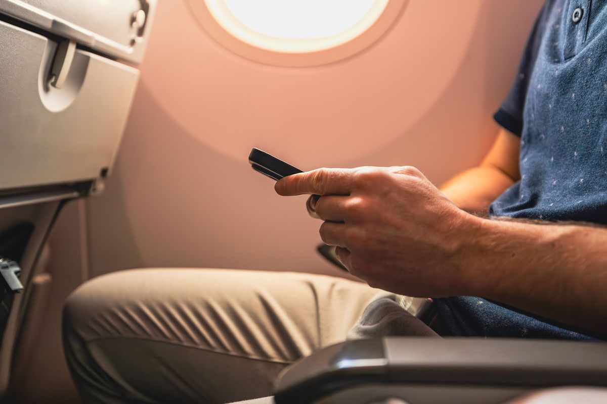 Close-up of man hand while using smart phone in airplane during flight