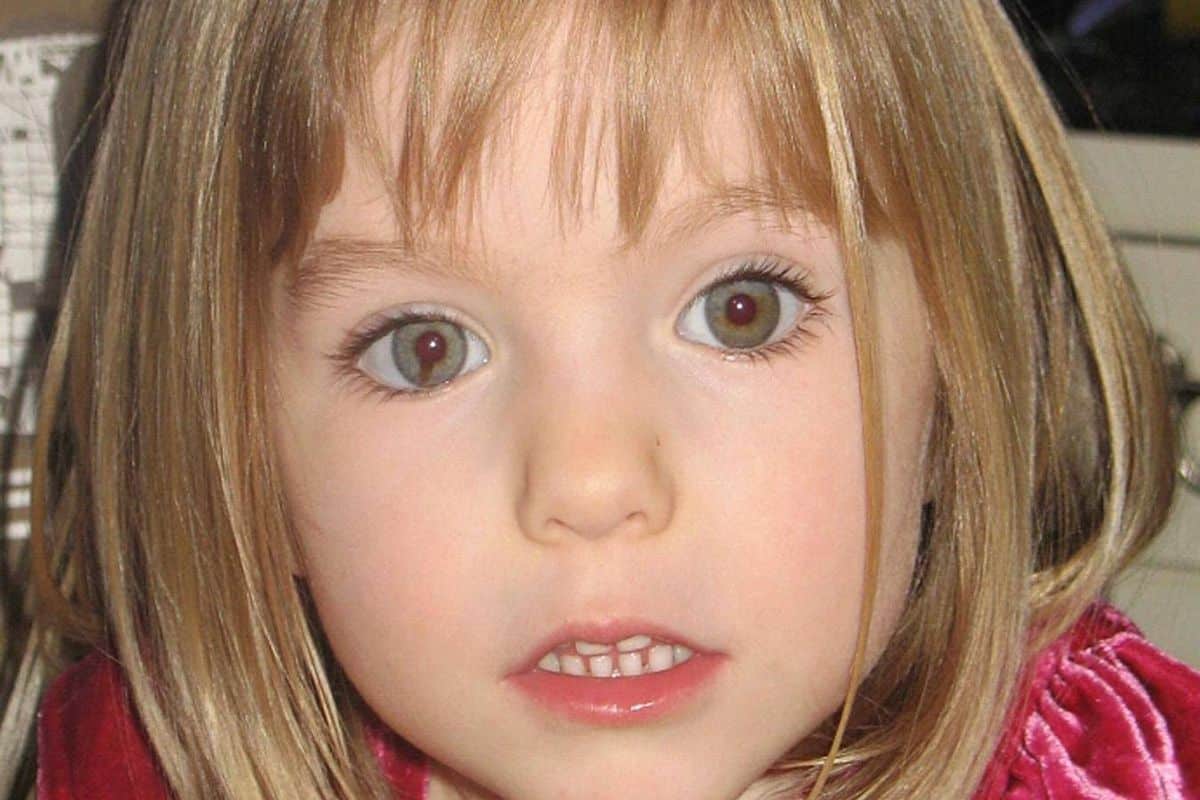 A young child with short, light blonde hair and blue eyes, wearing a red garment, appears to be in a contemplative pose, gazing forward with a slight expression of curiosity or surprise.
